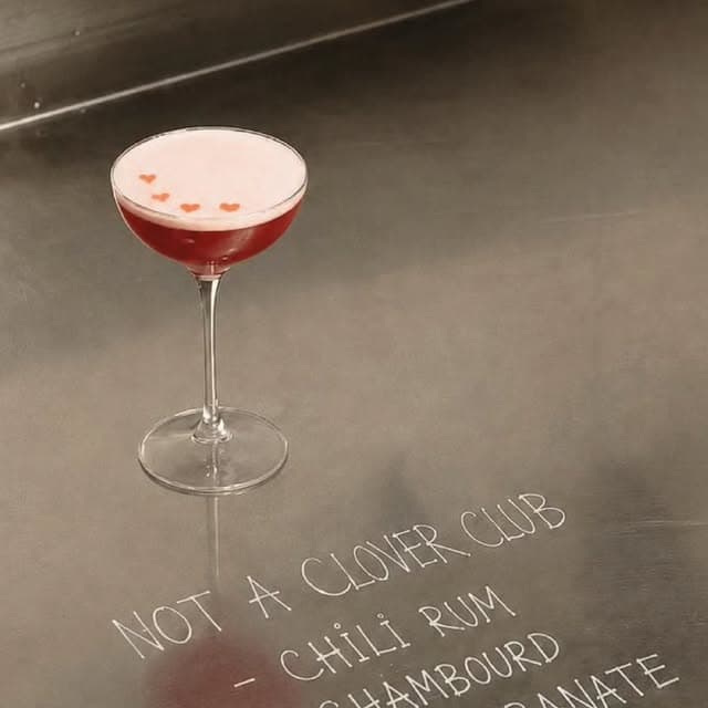 Cocktail rose en coupe, mousse claire et trois petits cœurs rouges
